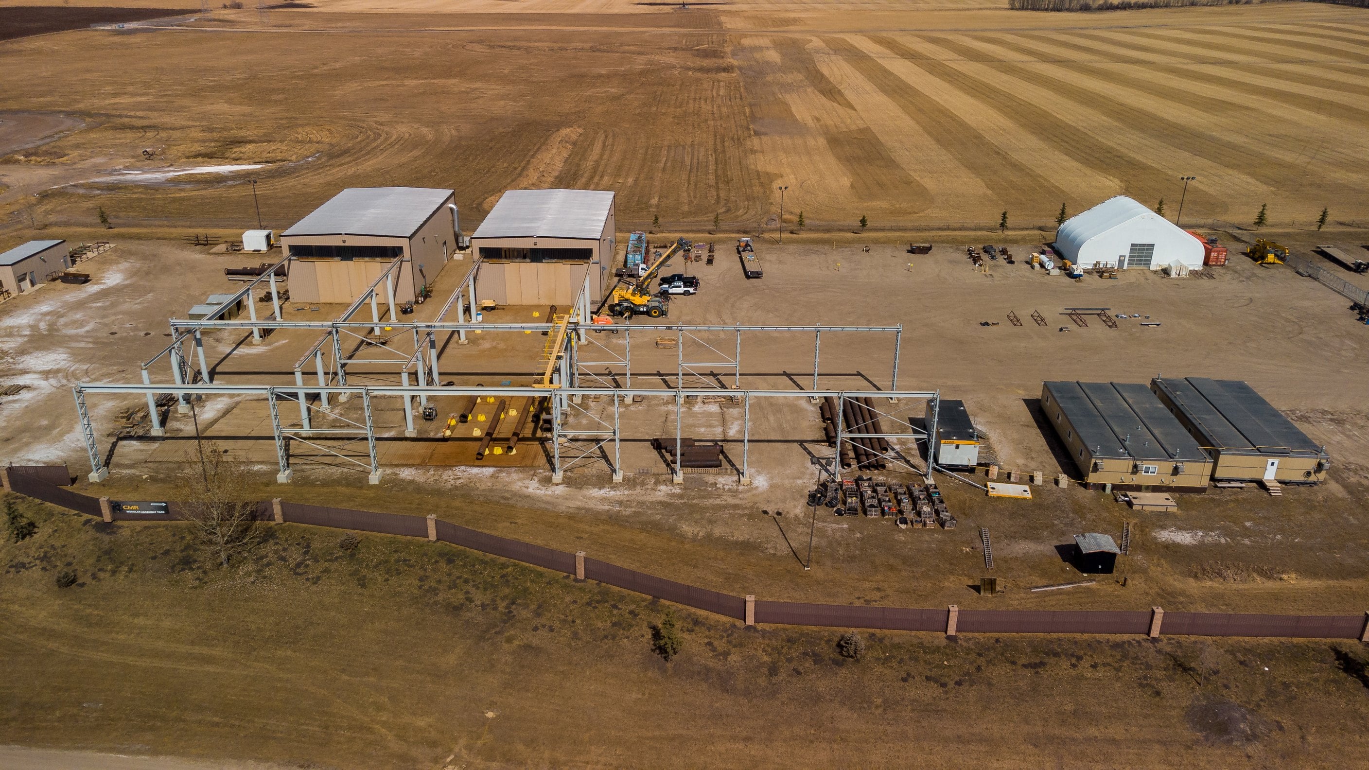 Aerial view of an industrial fabrication yard with steel frames and site buildings on the Alberta prairie.